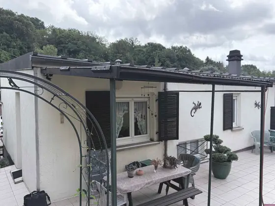 Betting avant travaux, côté terrasse : mur blanc et volets sombres sous la pergola